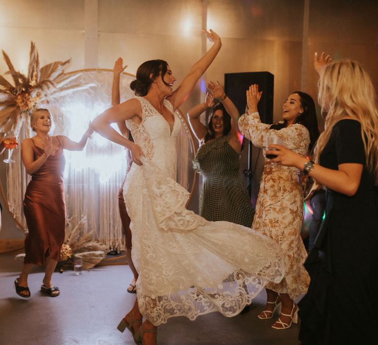 Bride in lace v neck wedding dress dances with wedding guests by neon wedding sign for barn wedding reception in Dorset