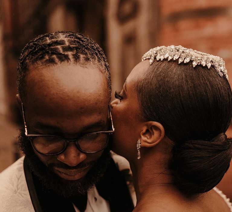 Black bride with a chic bridal up do kissing her grooms cheek 