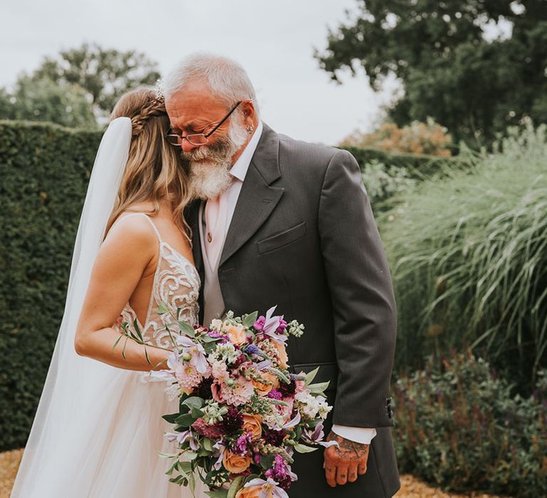 Bride holds brightly coloured wedding bouquet of purple, orange, pink and white flowers