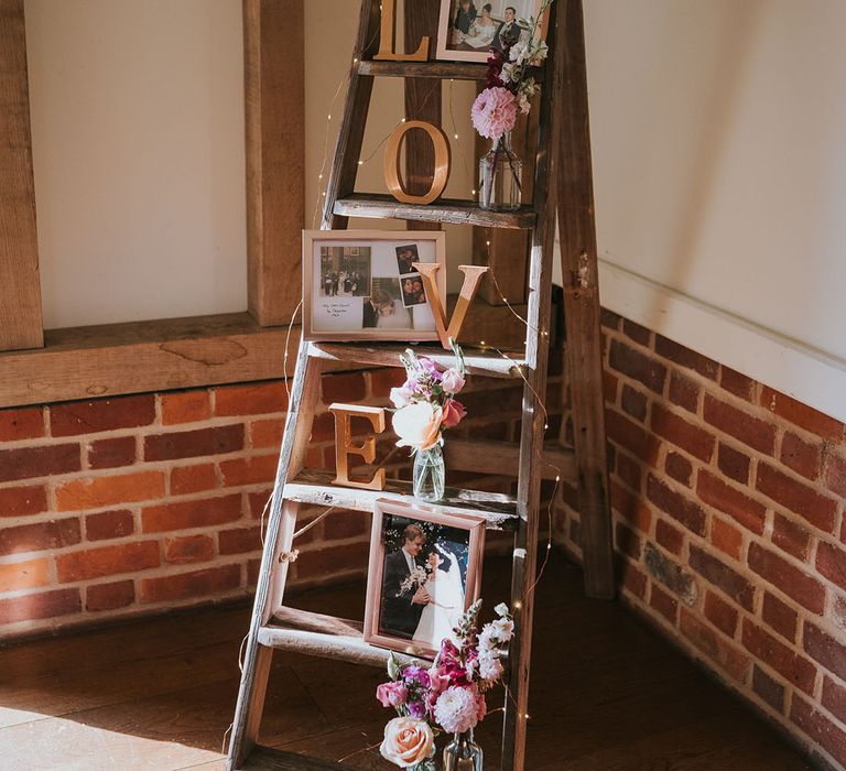 Wooden ladder rustic wedding decor with family photos and small vases of pink, red and white flowers