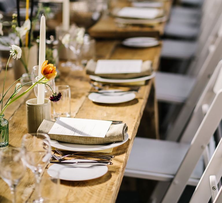 Long wooden banquet table with white plates, silver cutlery and fabric napkins with flower for table setting at country house wedding