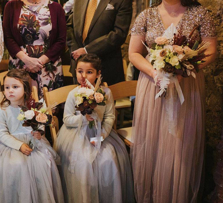 Flower girls in matching grey dresses with cardigans holding bouquet with light and dark flowers