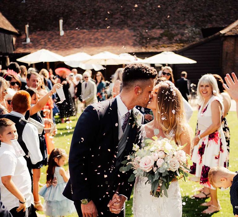 Bride in lace wedding dress kisses groom in three piece suit as they have their confetti exit after their ceremony