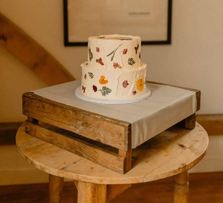 Two-tier white frosted wedding cake with pressed flowers decoration