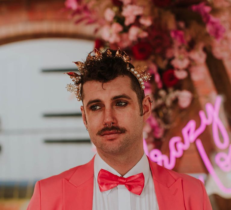 Groom in a pink suit and satin bow tie wearing a gold crown headpiece 