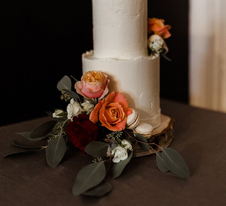 Two tier white buttercream frosted wedding cake decorated with roses and white macaroons