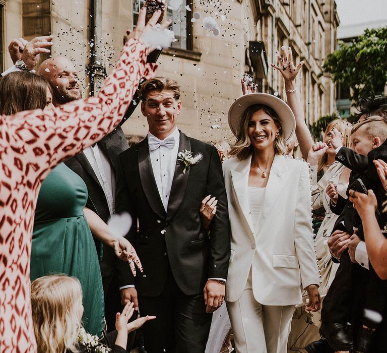 Bride in pearl Nadine Merabi trouser suit and groom in black tie with blue bow tie 