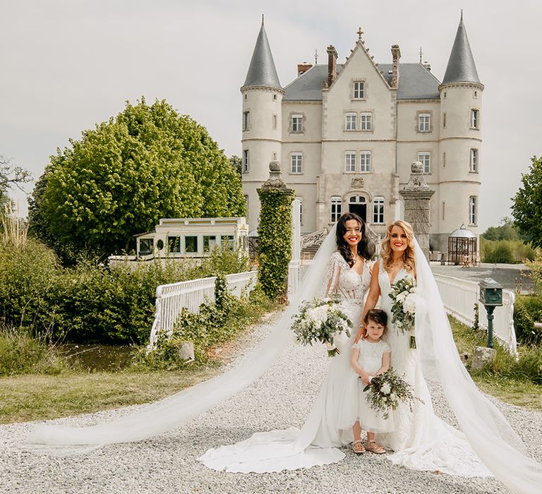 Brides pose with the flower girl all holding classic white wedding flower bouquets and pretty lace wedding dresses 