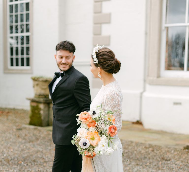 Black tie wedding with groom in a tuxedo and bride in an embellished wedding dress with chic up do holding a peach and white wedding bouquet 