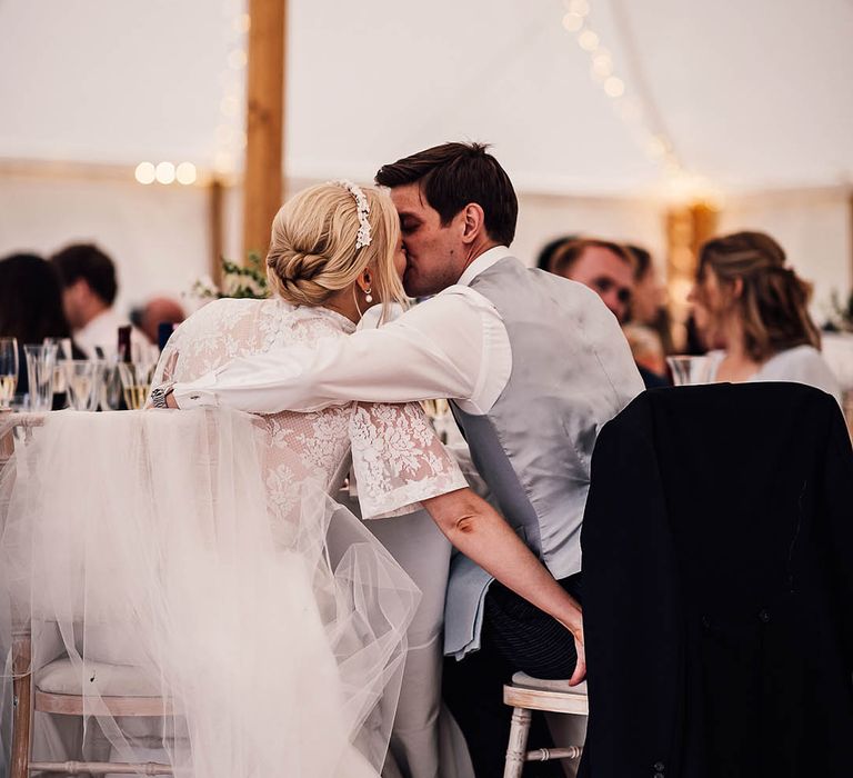 Bride and groom share a kiss as they are seated at the table for their reception 