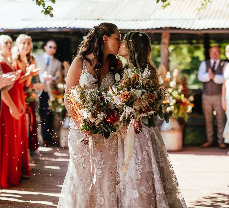 Brides share a kiss as they have a confetti moment after their wedding ceremony 