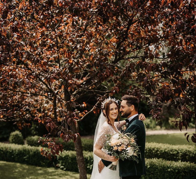 Groom in a velvet green custom suit jacket with the bride in a dotted wedding dress with a crown and pearl jewellery