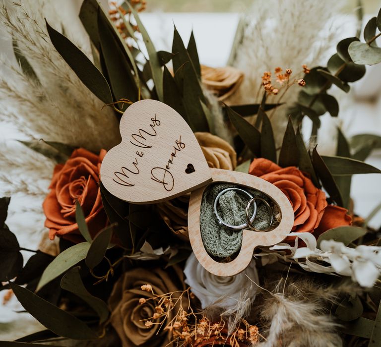 Mr and Mrs Dennis wooden heart shaped ring box on top of the neutral themed dried flower bouquet with burnt orange roses