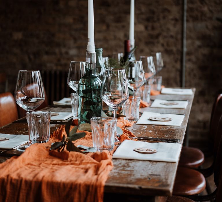 Burnt orange fabric table runner on wooden table with white candles 