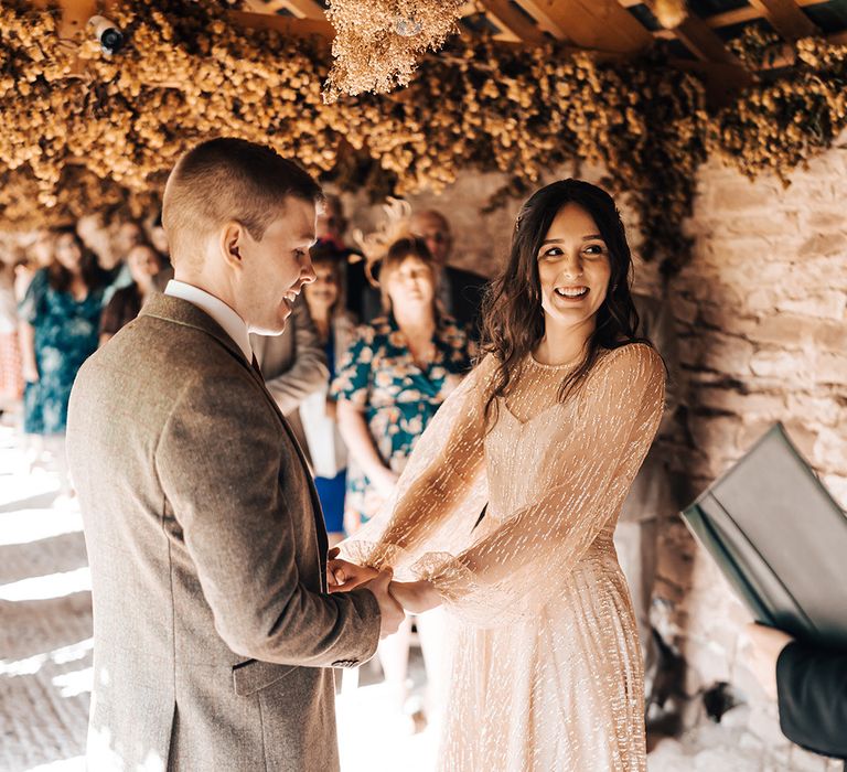 Bride in long sleeve sheer gold wedding dress stands with her groom during Lyde Court wedding ceremony