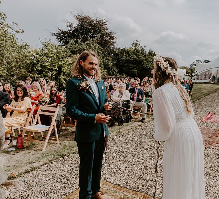 Bride & groom during handfasting ceremony outdoors on their wedding day with boho feel 