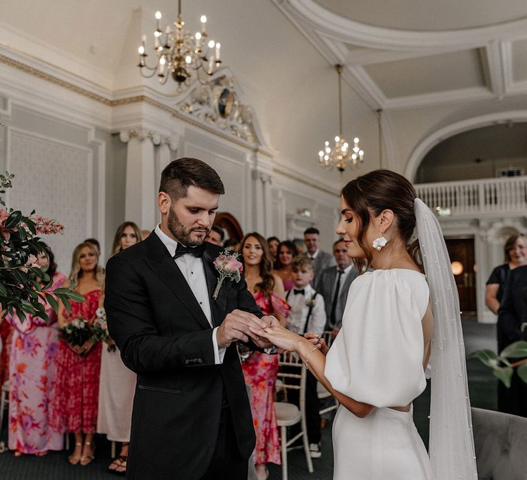 Bride in puff sleeve wedding dress with open back detail and groom in dark tux exchanging rings at the alter of Somerset House