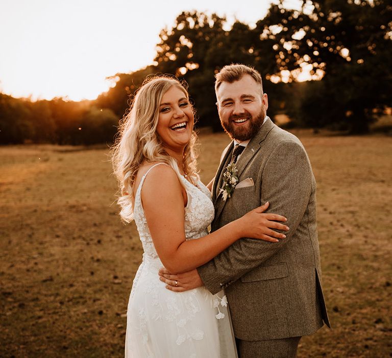 The bride with curled blonde hair laughs with the bearded groom for their cute couple portraits 