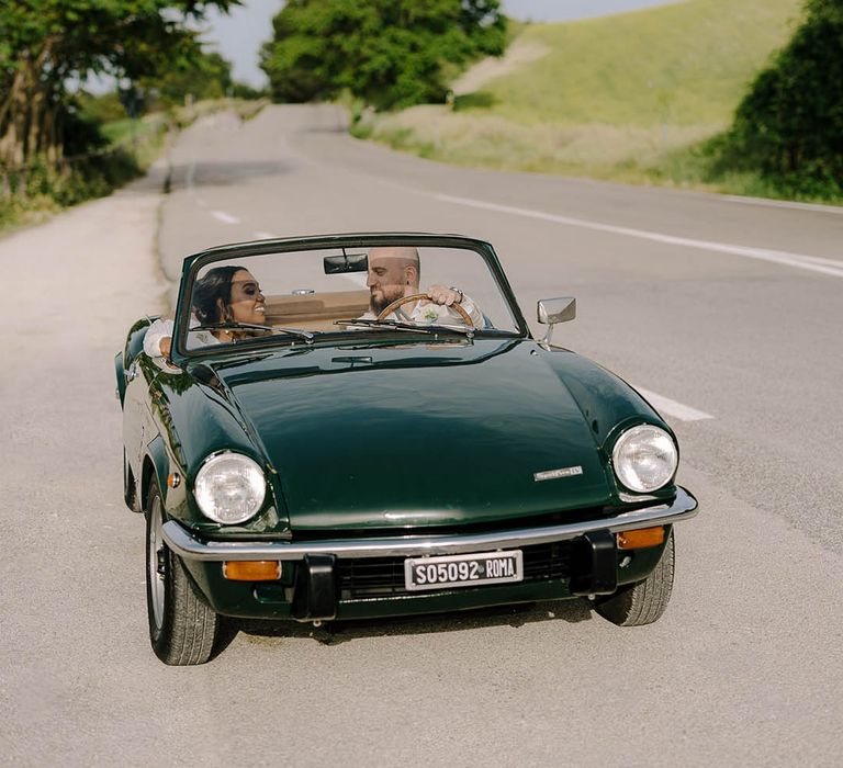 Bride and Groom smiling at each other whilst driving a vintage Alfa Romeo Spidee through Italy