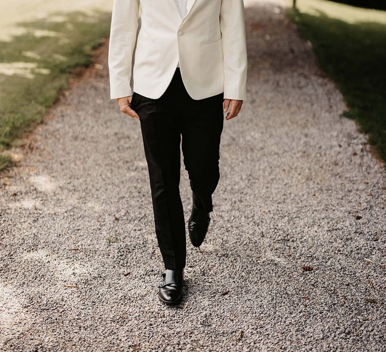 Groom in black suit trousers, white suit jacket, black bow tie, and white rose buttonhole 