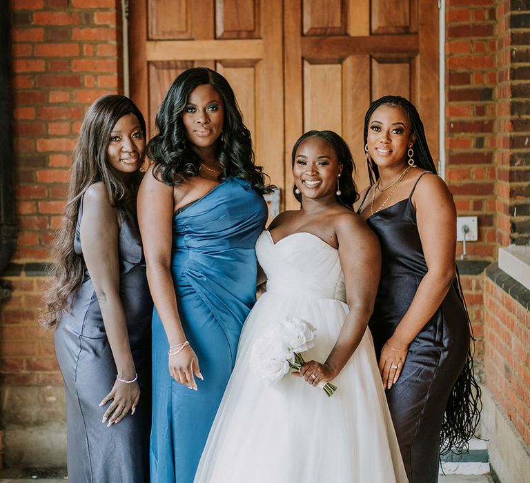 Black bride in strapless wedding dress smiling with her bridesmaids in blue and black dresses in a satin slinky material