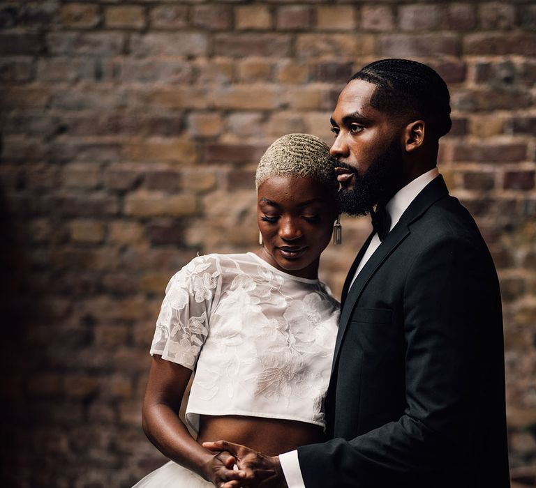 Bride and Groom dance at 100 Barrington in front of exposed brick. The Bride wears a floral and ruffled bridal two piece set