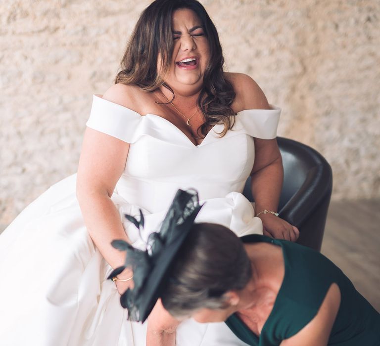 Mother of the green in emerald green dress and fascinator with the bride in an off the shoulder wedding dress wearing blue pointed heels with jewelled front