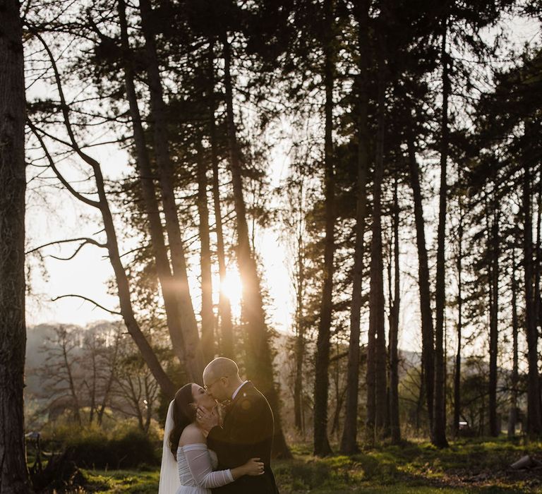 Golden hour sunset wedding photo of the bride and groom kissing in the woodland at Brinsop Court Manor House and Barn