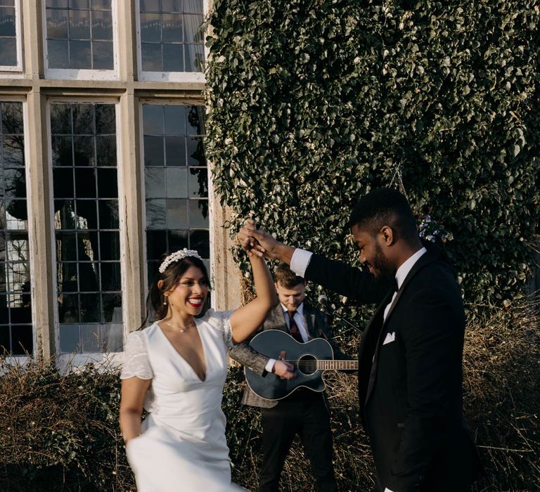 Bride in v neck short sleeve wedding dress and groom in classic black tuxedo dancing outside Yorkshire wedding venue with live wedding band outside 