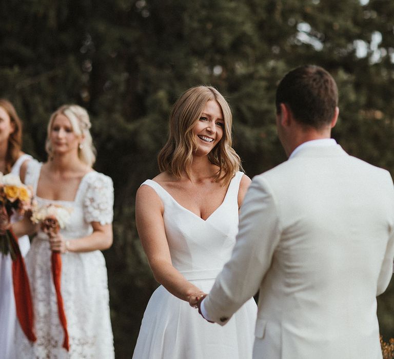 Bride in Suzanne Neville wedding dress looks lovingly toward her groom during outdoor wedding ceremony 