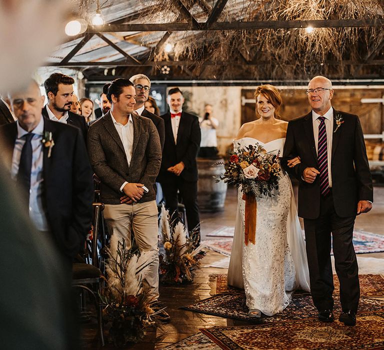 Bride in Love Spell wedding dress walks down the aisle across Moroccan styled carpets in The Dreys barn wedding venue 