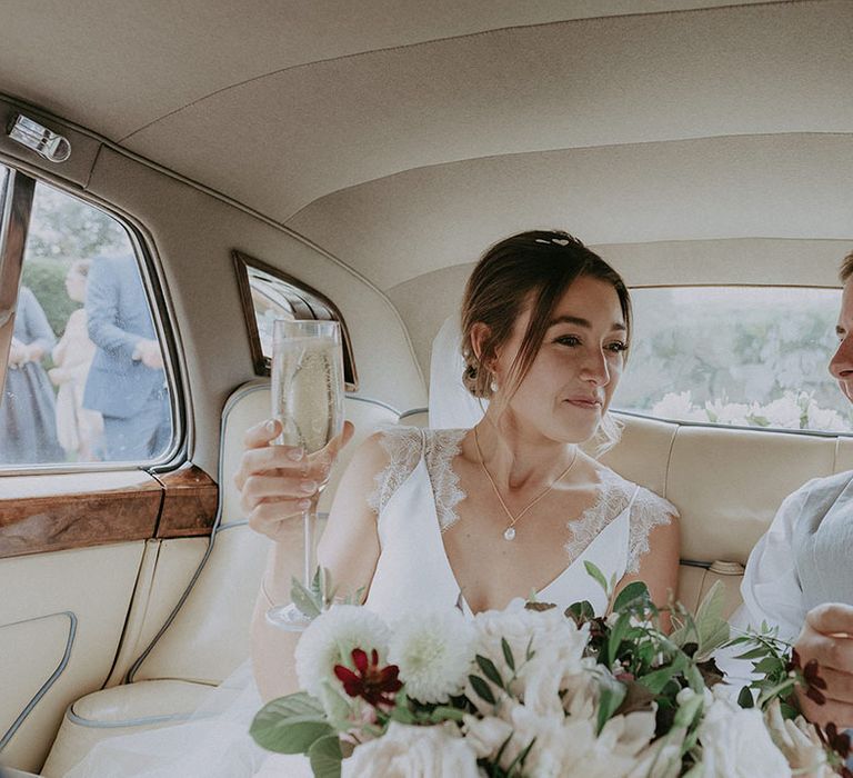 Bride holds champagne alongside her groom in vintage wedding car 