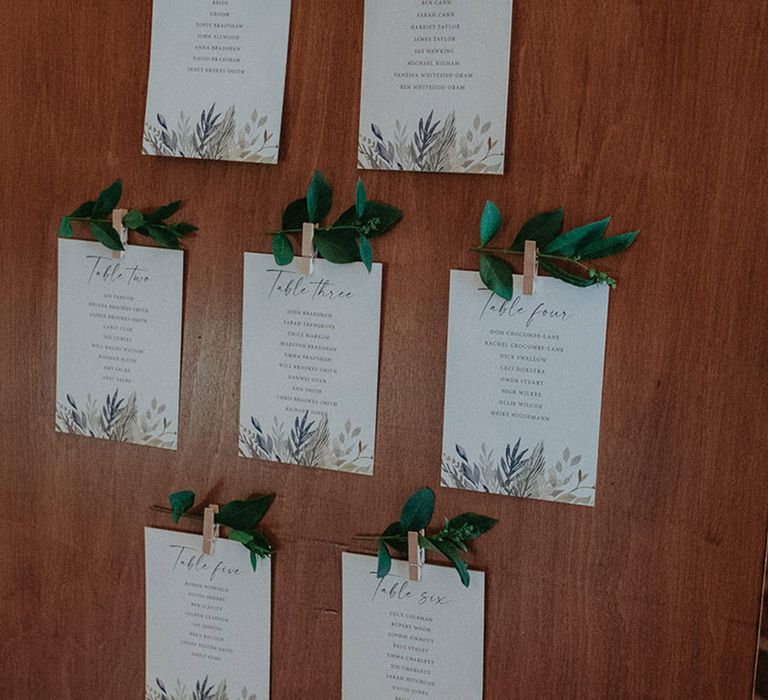 Wooden table plan with small cards attached with pegs listing the guest's names with leaves for decoration 