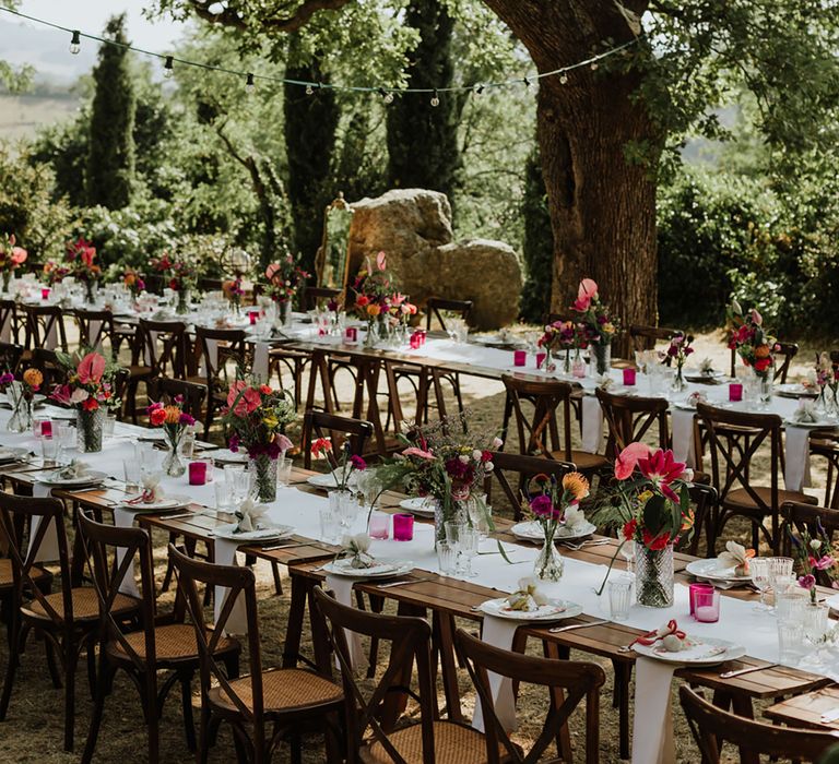 Banquet-style tables at outdoor woodland wedding with rustic colourful tablescape