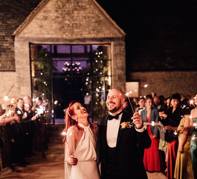 Bride in Halfpenny London wedding dress with pearl wedding cape walking with the groom during a sparkler send off