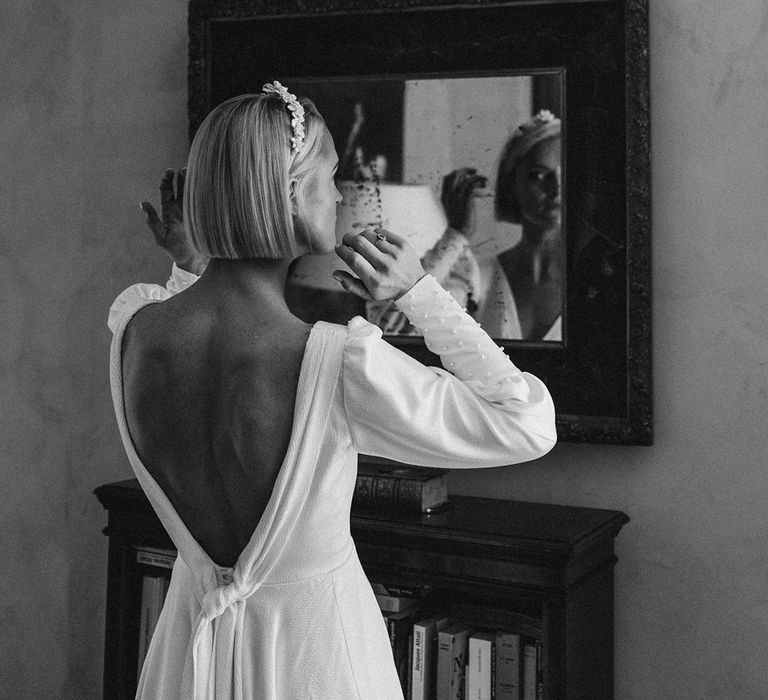 bride with short bob hair and low back wedding dress looking at herself in the mirror on the wedding morning 