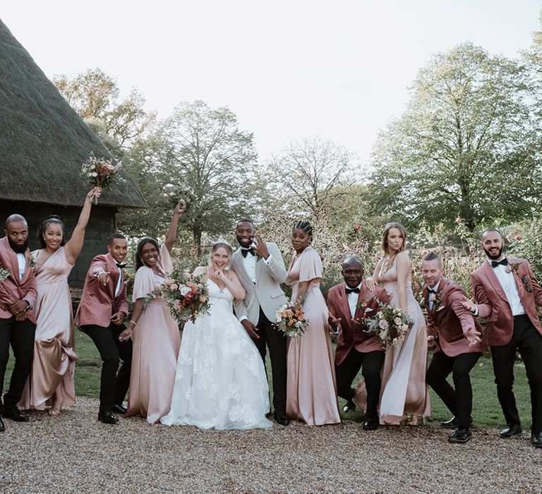 Bridesmaids in satin blush pink bridesmaid dresses with the groomsmen in blush pink velvet suits smiling with the bride and groom 