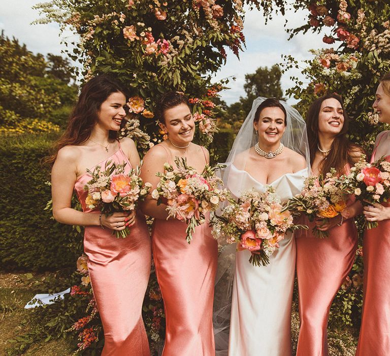 Bridal party in Pretty Lavish pink bridesmaid dresses with the bride holding matching bouquets wearing pearl choker necklace 