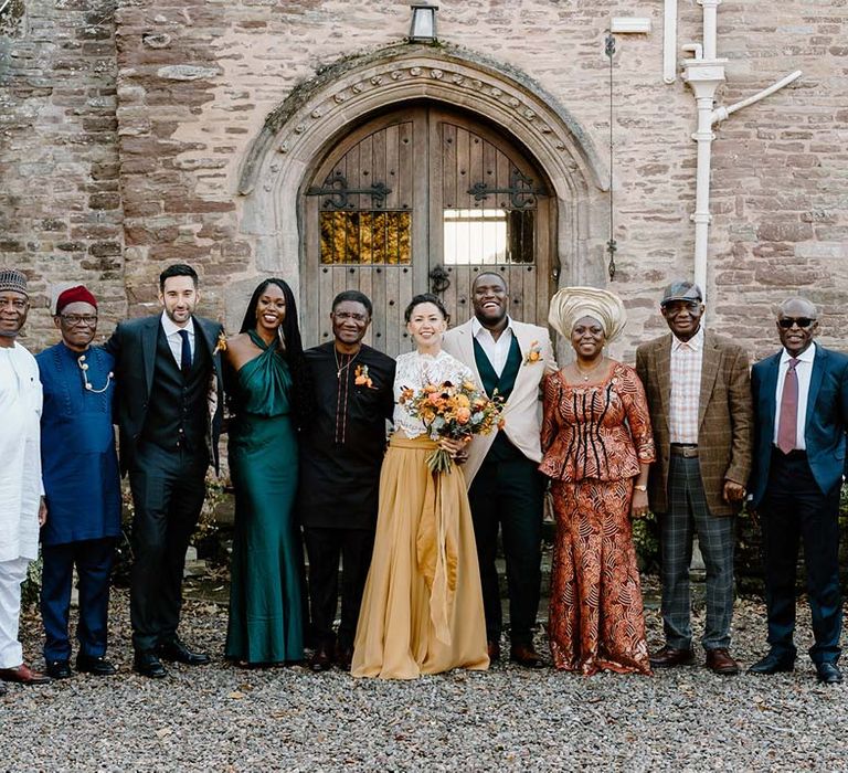 Wedding party standing with bride in white mesh lace bridal crop top and yellow wedding skirt holding dried autumnal wedding bouquet with sunflowers, garden roses, pampas grass, eucalyptus, yellow tall kangaroo paws, orange osmanthus flowers, foliage and dried flowers standing outside of Broadfield Court wedding venue