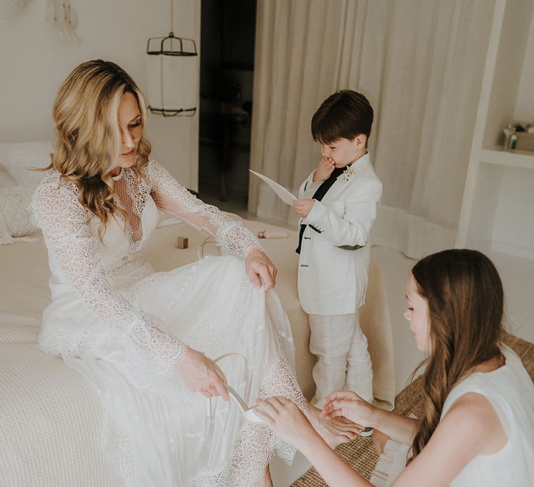 bride in a long sleeve lace wedding dress putting on her wedding shoes