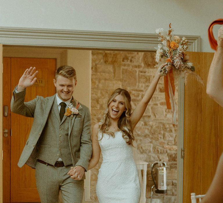 Bride in a fitted lace wedding dress walking into the wedding reception holding hands with the groom at St Tewdrices House Chepstow 