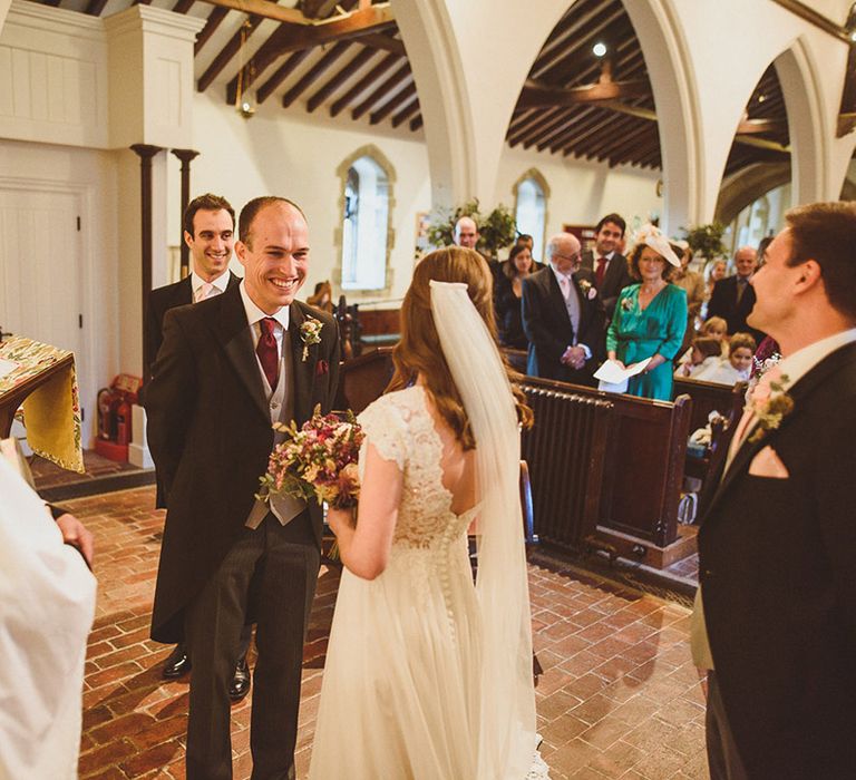 The bride and groom smile at each other as they stand at the altar 