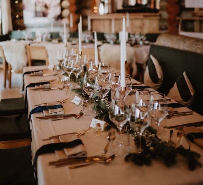 La Cabane Des Praz wedding venue reception room with classic wedding tablescape with forest green napkins, white wedding tablecloth, white tapered candles and minimalistic wedding stationery and menus