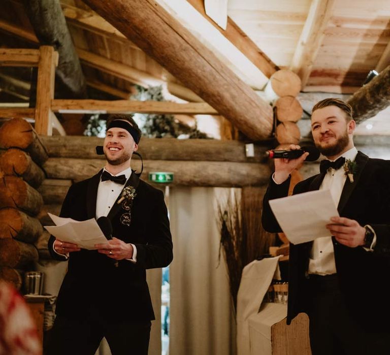 Groomsmen wearing classic black groomsmen tuxedos with black bowties doing funny wedding speeches at destination French ski wedding