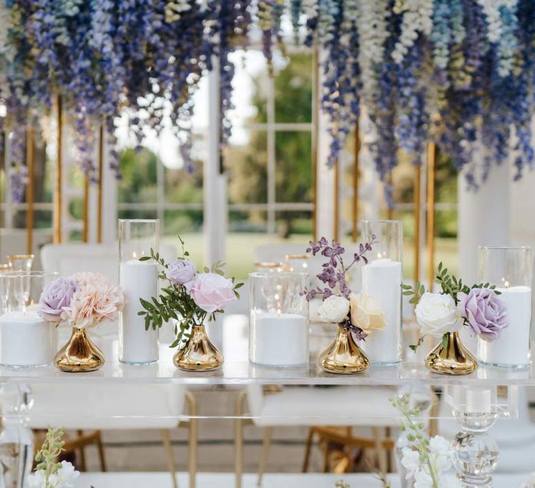 Wedding top table with hurricane vases and pillar candles, gold flower vases, pastel flower centrepieces and pastel and foliage flower arrangements 