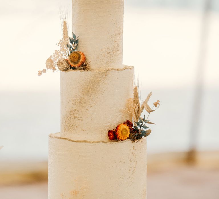 Three tier white frosted wedding cake with dried orange wedding flowers decorating the cake 