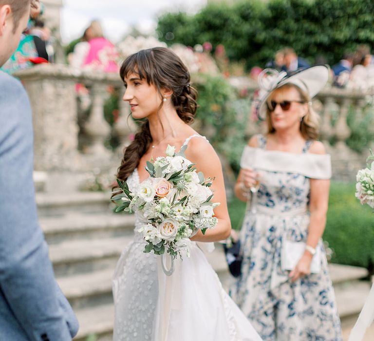 elegant bride in a Made With Love wedding dress with fitted bodice and floaty skirt holding a white summer bouquet 