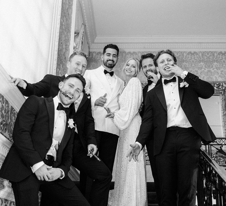 Groomsmen in black tuxedos with cigar with bride and groom in their wedding reception outfits 