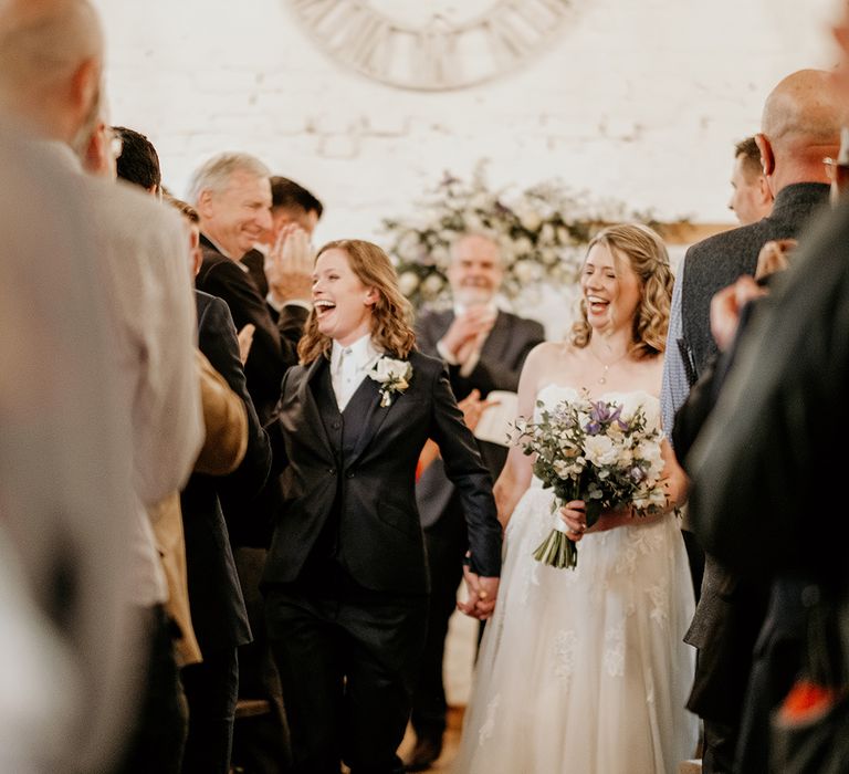 two brides descending up the aisle at Stanford Farm wedding in a navy suit and strapless lace wedding dress