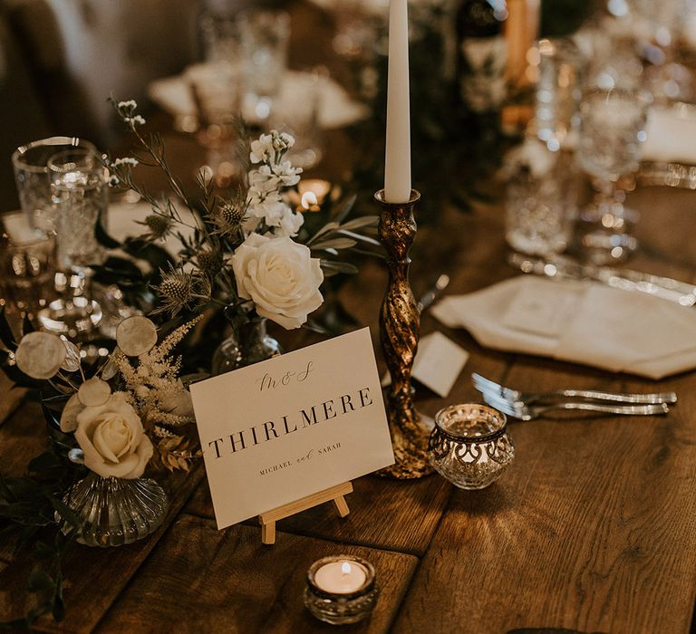 Minimalist and classic black and white wedding table name sign siting next to traditional white wedding flower arrangements for the table 